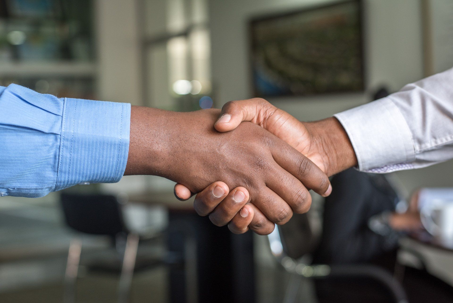 Two people shaking hands in an office, one in a blue shirt and one in a white shirt.