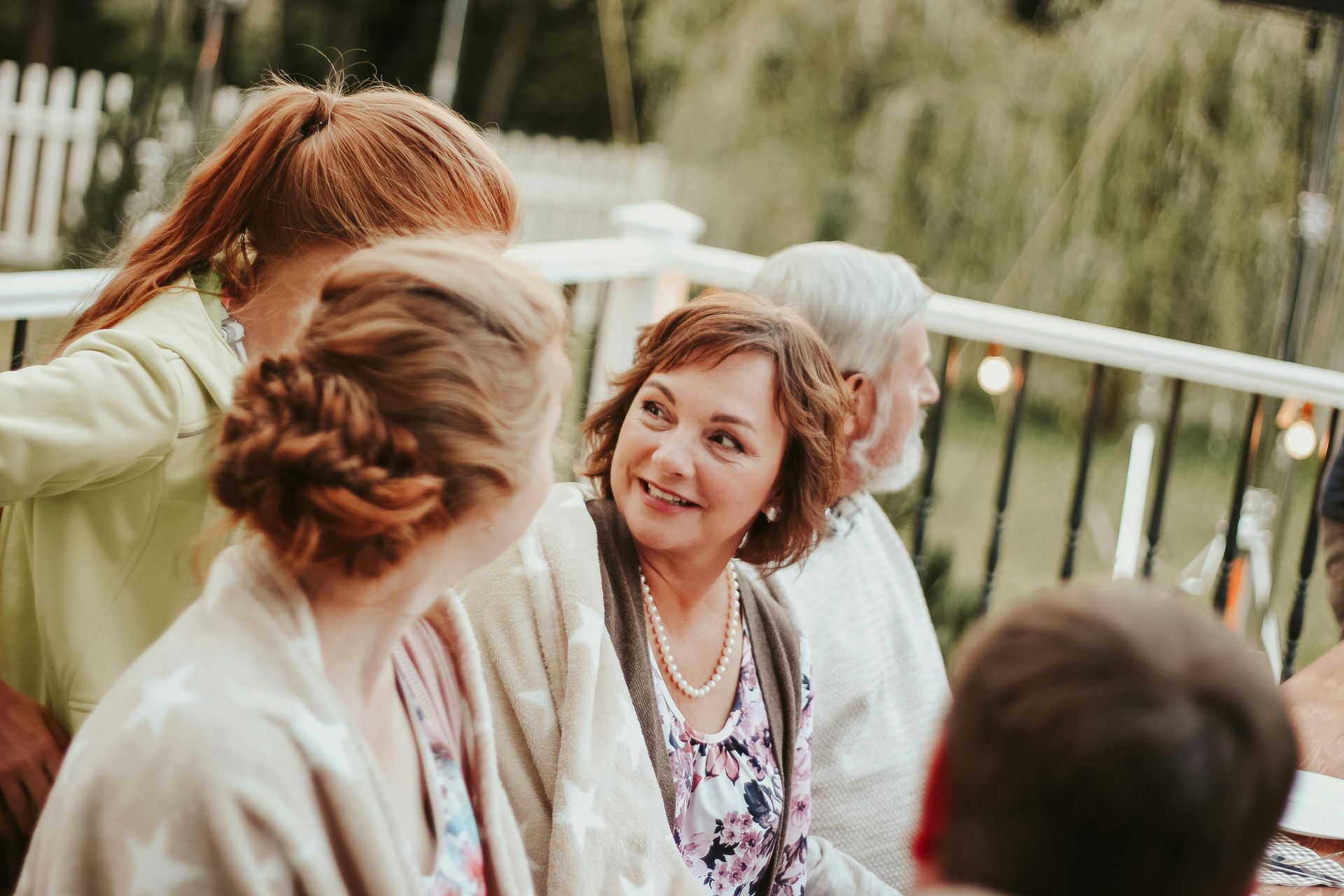 People seated outdoors in conversation, with a woman in a floral top centered in the foreground