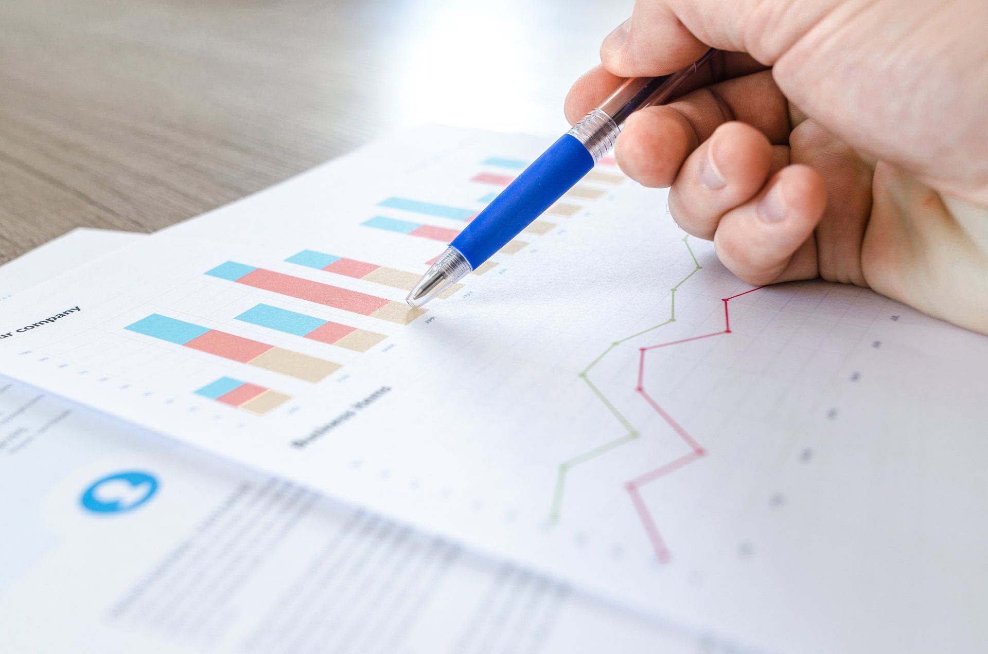 Hand holding blue pen over printed charts and graphs on a desk