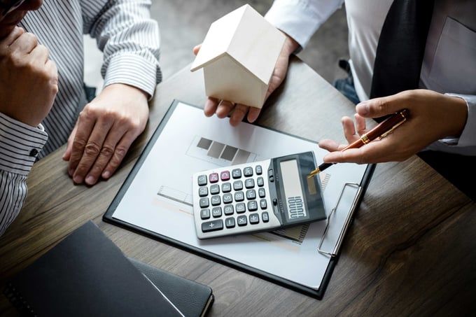 Hands around a calculator and house model on a desk during a financial planning meeting