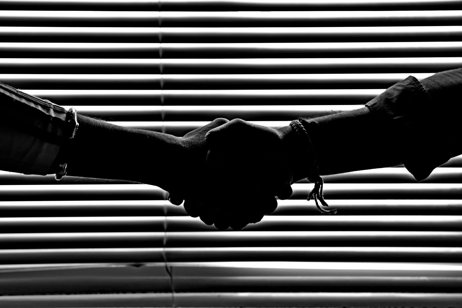 Silhouetted hands shaking in front of horizontal window blinds